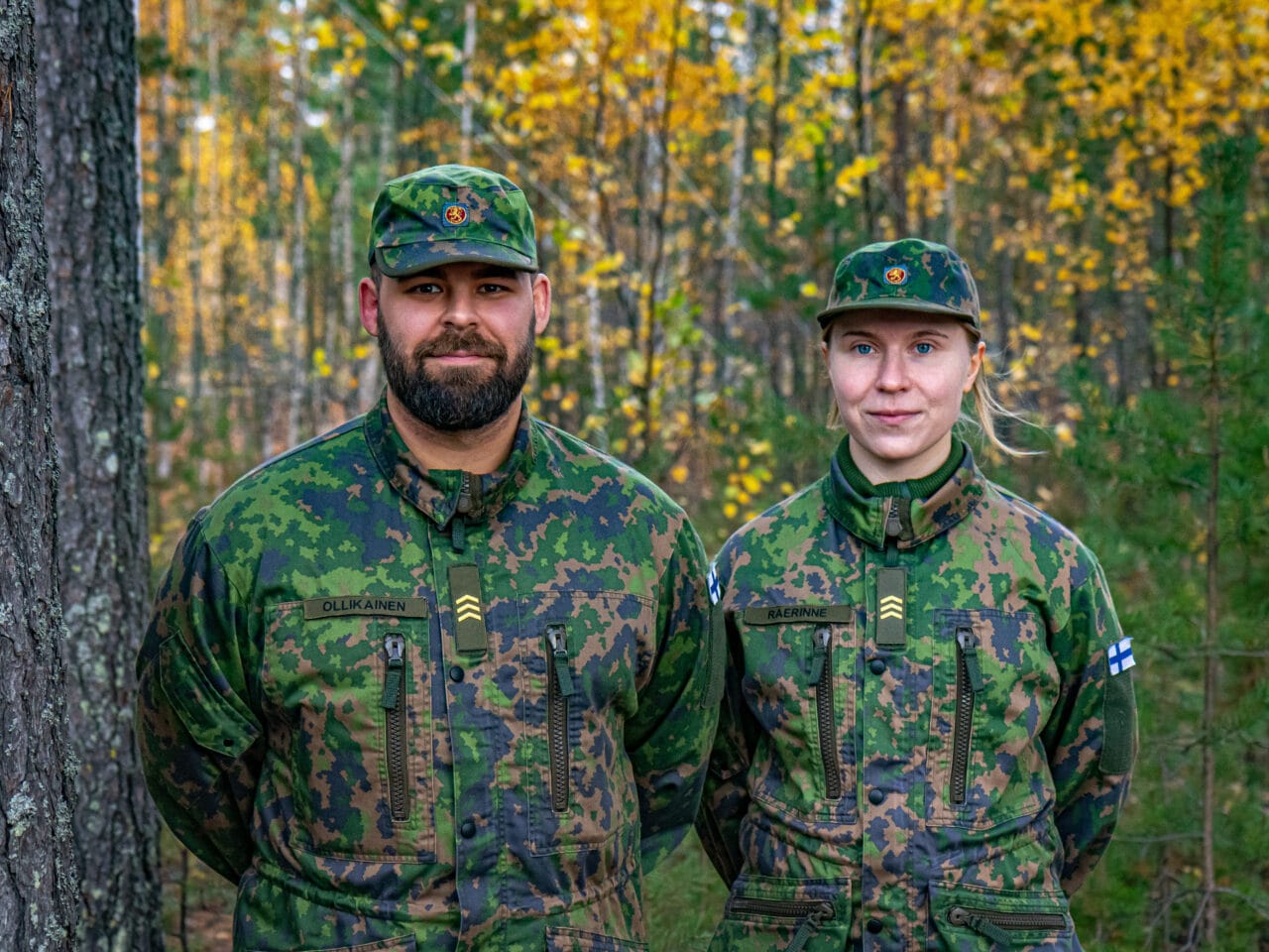 Kuvassa kaksi maastopukuista henkilöä. Vasemmalla Jussi Ollikainen ja oikealla Elina Raerinne. Kumpikin katsoo kameraan ja hymyilee. Taustalla syksyinen metsämaisema.