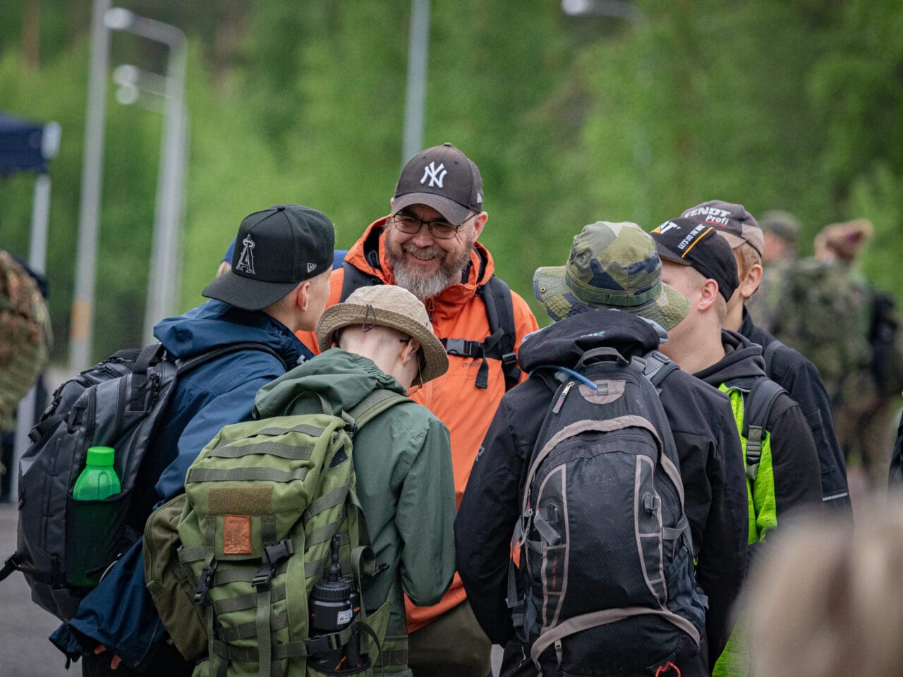 Kuvassa ulkovaatteisiin pukeutuneita nuoria lähdössä marssille ohjaajansa, oranssitakkisen miehen kanssa. Henkilöt juttelevat keskenään ympyrän muodossa, nuoret selkä kameraan päin. Miehen kasvot näkyvät ja hän hymyilee iloisesti.