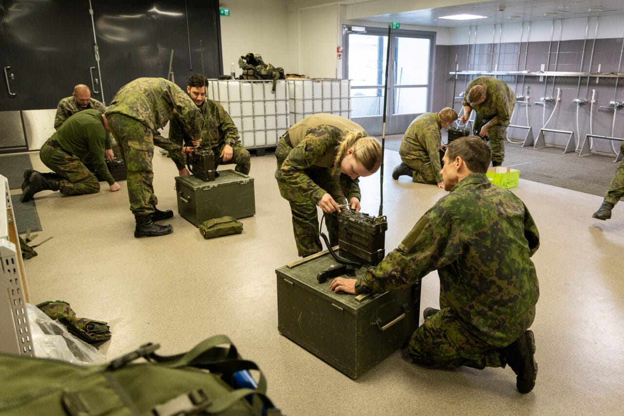 Maastopukuiset ihmiset ovat kerääntyneet lattialla olevan laitteen ympärille.