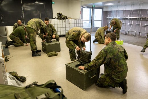 Maastopukuiset ihmiset ovat kerääntyneet lattialla olevan laitteen ympärille.