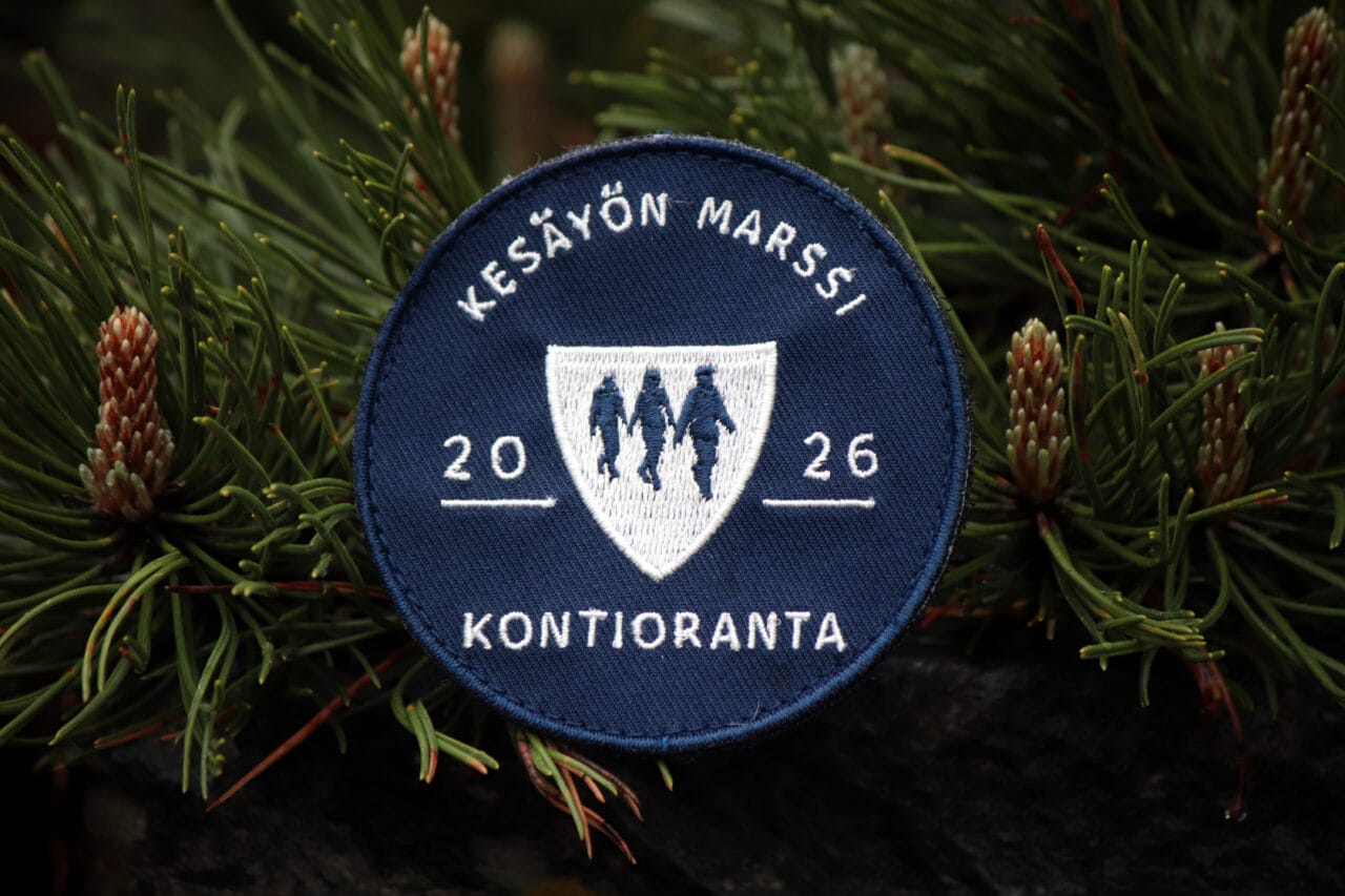 Kuvassa sininen Kesäyön marssi Kontioranta 2026 -velcromerkki lähikuvassa, taustalla havupuun oksia.