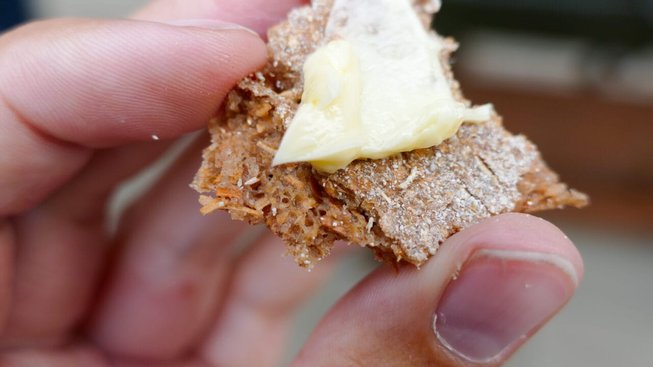 Lähikuva pettuleivästä, jota henkilö pitää käsissään. Leipä muistuttaa vaaleaa ruisleipää ja sen päällä on reilusti voita.