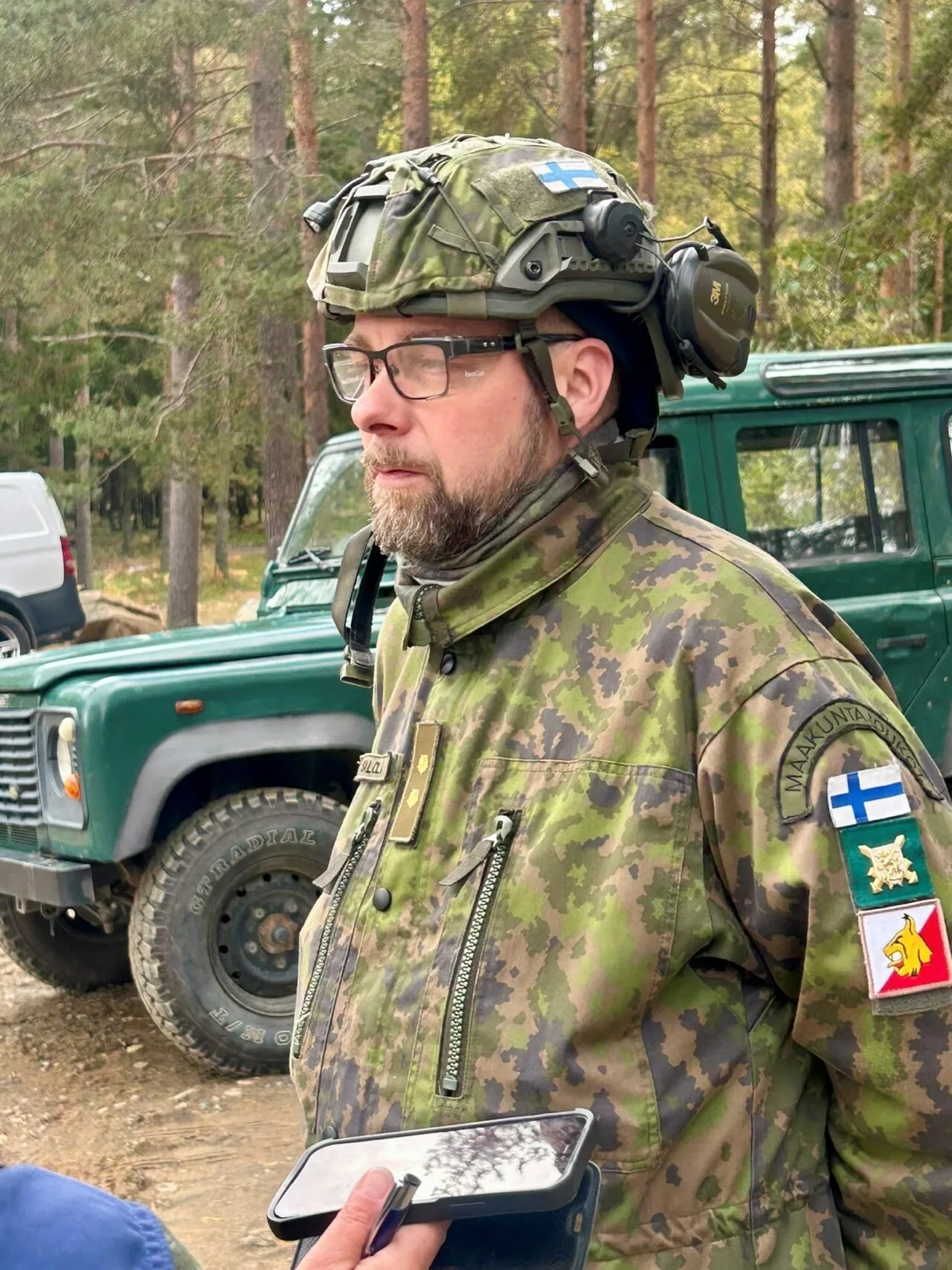 Sotilasasuinen mies jeepin edessä